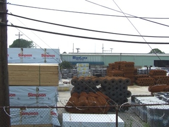 A gravel lot with a large amount of construction materials in it including rolls of metal fencing and stacked wood.