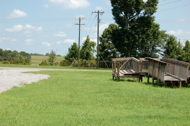 A grassy field with an old, broken, wooden platform to the right in a grassy field with two wooden power poles and a large tree to the right.