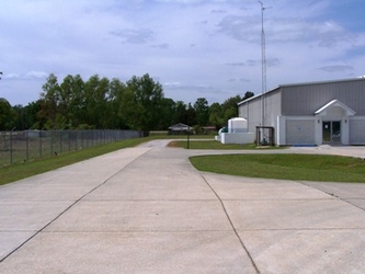 A large concrete driveway with a chain link fence to the left and a large metal building to the right.