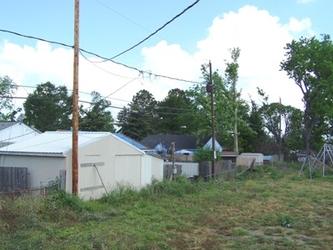 A small tan building behind an electricity pole and wires with a grassy field in front.