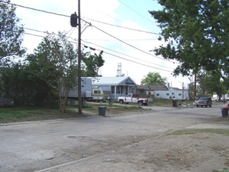 A neighborhood street with a paved driveway in the foreground and houses in the background with electricity lines and trees throughout the yards.