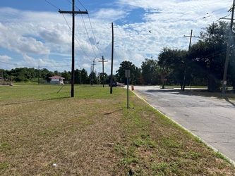 A road on the right side and grass field on the left side with electrical poles lining the road and a cloudy sky overhead.