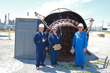 Three inspectors wearing safety gear standing in front of a large flare tip that is lying on the ground
