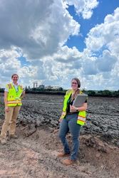 Two female inspectors wearing bright green safety vests standing in front of sloped land covered in mud