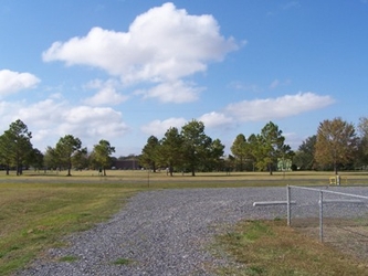 A curving gravel road, some fencing, and trees in the distance.