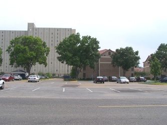 A large parking lot with cars sparsely parked in spots; trees and buildings are in the background.