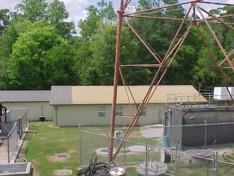 Large trees in the background with a tan colored building in the center and a gray building to the right.