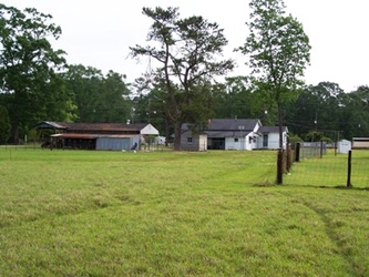 A grass yard with houses and trees in the background and some fencing on the right.