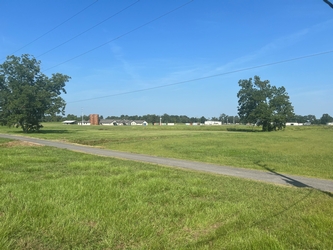 An expansive grass field with a paved path running horizontally through the middle. There are houses and trees in the background.
