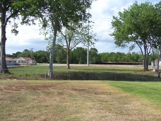 A dirt path flanked by short grass with trees in the center and background of the view.