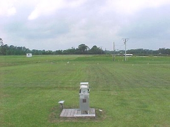 A piece of equipment in the center foreground of a grass field with a cloudy sky overhead and trees on the horizon.