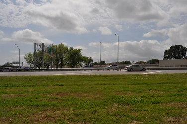 An interstate highway with cars going horizontally through the middle with grass in the foreground and a cloudy sky in the background.