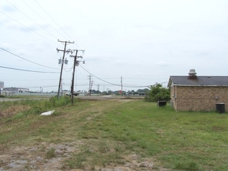 A grass and dirt field with a small brick building to the right and electrical poles and wires on the left.