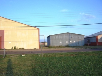 Grass in the foreground, a road running horizontally across the center, and three buildings filling the background under a clear blue sky.