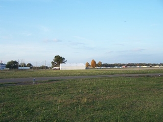 A lush grass field with a road running horizontally across the center; buildings and trees are in the far background.
