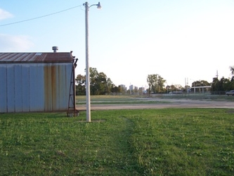 Grass in the foreground, bare ground in the center, a metal building and electrical pole to the left, and trees in the far distance.