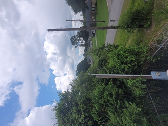 An electrical pole and top of a tree in the foreground, and a residential area of homes, yards, and roads in the background under a cloudy sky.